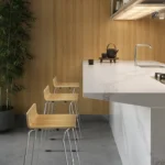 Minimalist kitchen with marble island, wooden bar stools, built-in stove, and large potted plant.
