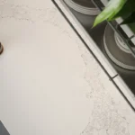 Teapot, cup of tea, leaf plant, plates, and chair on a white marble tabletop.