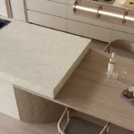Caesarstone ICON 8251 Taj Whisper Kitchen with modern kitchen with marble island, wood dining table, chairs, fruit bowl, and water bottle.